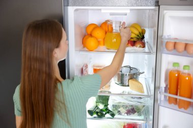 Mutfaktaki buzdolabından portakal suyu alan kadın.