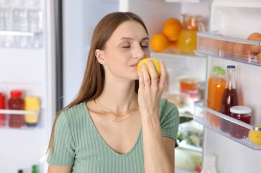 Mutfakta açık buzdolabının yanında limonlu bir kadın.