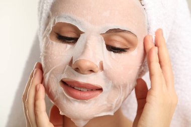 Saçları havluya sarılı ve açık gri arka planda maske takan kadın, yakın plan.