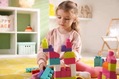 Küçük kız oyun odasında yerde oyuncaklarla oynuyor.