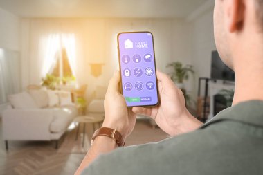Akıllı ev sistemi. Oda özelliklerini kontrol etmek için cep telefonundaki uygulamayı kullanan adam, yakın plan
