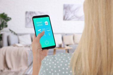 Akıllı ev sistemi. Oda özelliklerini kontrol etmek için cep telefonundaki uygulamayı kullanan kadın, yakın plan