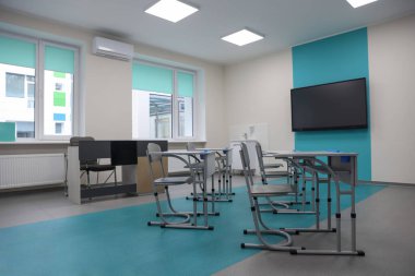 Okulda masaları, sandalyeleri ve televizyonu olan şık bir sınıf.