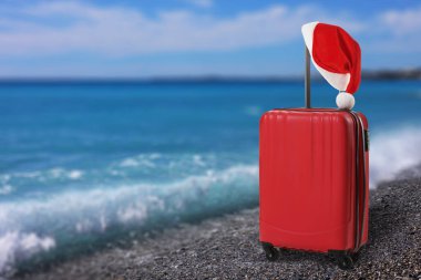 Noel tatili. Deniz kıyısında Noel Baba şapkalı bavul.