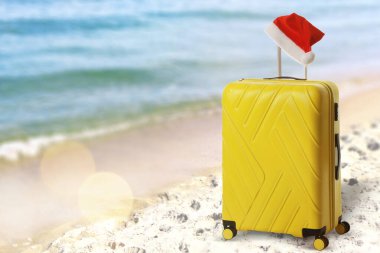 Noel tatili. Okyanus kıyısındaki kumlu sahilde Noel Baba şapkalı çanta.