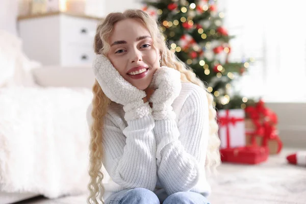 Evdeki bulanık ışıklara karşı eldivenli ve kazaklı gülümseyen kadın portresi. Mutlu Noeller ve mutlu yıllar.