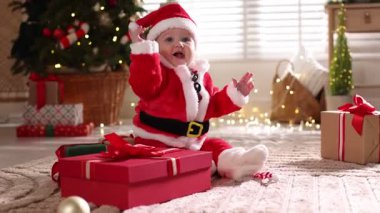 Noel Baba kostümlü şirin bir bebek ve evde yerde Noel hediyeleri.