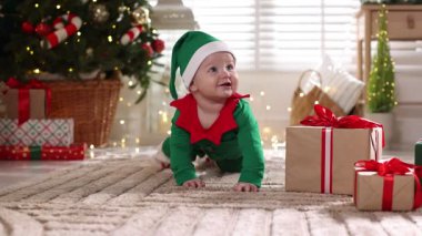 Evde yerde elf kostümü giymiş şirin bir çocuk var. Bebeğin ilk Noel 'i