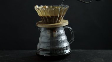 Sıcak suyu cam kimya kahve makinesine döküyorum filtresi ve siyah masaya öğütülmüş kahve, yakın plan.