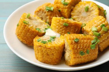 Kaynamış mısır koçanı parçaları yeşil soğan ve tereyağı ile açık mavi ahşap masa, yakın çekim