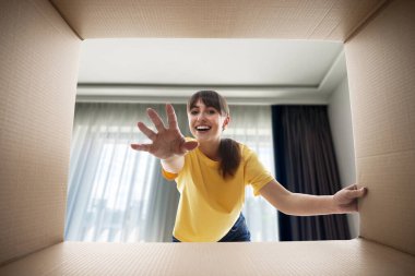 Kadın odada karton kutuya bakıyor, içeriden bakıyor.