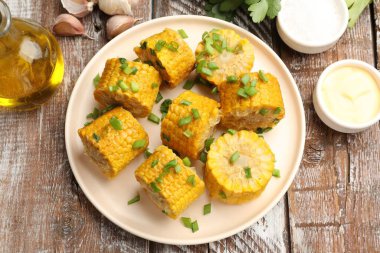 Haşlanmış mısır koçanları ve yeşil soğan. Tahta masada servis ediliyor.