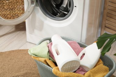 Çamaşır sepetinde havlular ve çamaşır makinesinin yanında şişe deterjan var.