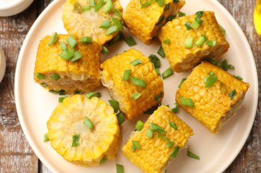 Ahşap masada yeşil soğanlı haşlanmış mısır koçanı parçaları.