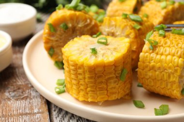 Ahşap masada yeşil soğanlı haşlanmış mısır koçanları, yakın plan.