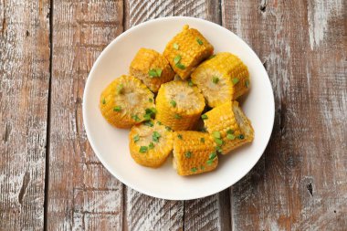 Ahşap masada yeşil soğanlı haşlanmış mısır koçanı parçaları.