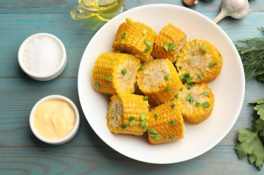 Kaynamış mısır koçanı parçaları ve yeşil soğan açık mavi ahşap masa üzerinde servis edilir.