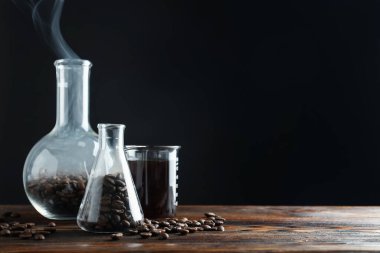 Kahve, fasulye ve beher dumanlı cam mataralar siyah arka plana karşı ahşap masada, yakın plan. Metin için boşluk