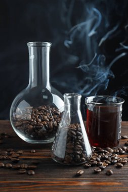 Kahve, fasulye ve beher dumanlı cam mataralar ahşap masada, yakın plan.