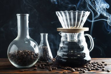 Kahve, fasulye ve labaratuar bardaklı cam kahve makinesi ahşap masada siyah arka planda, yakın planda.