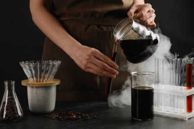 Siyah masada cam test tüpüne damlatan kadın, yakın plan.