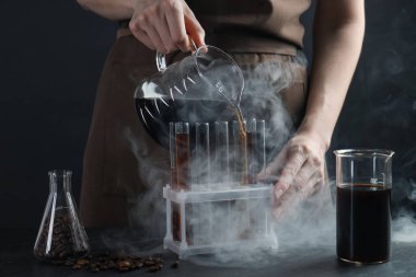 Siyah masada cam test tüpüne damlatan kadın, yakın plan.