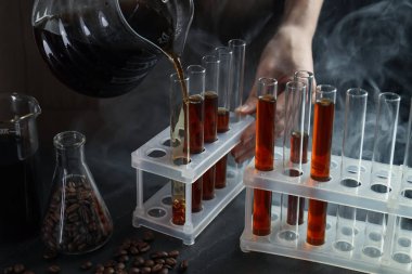 Siyah masada cam test tüpüne damlatan kadın, yakın plan.