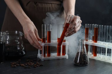 Elinde cam test tüpleri olan kadın kahve, fasulye ve sigara siyah masada, yakın plan.