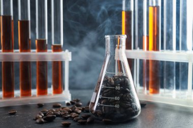 Kahve, fasulye ve dumanlı laboratuvar bardakları siyah masada, yakın plan.