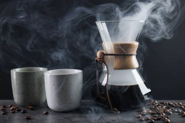 Cam kimya kahve makinesi, lezzetli kahve, fasulye ve fincanlar gri masada, yakın plan.