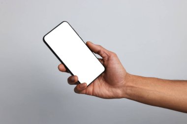 Açık gri arka planda boş ekranlı akıllı telefon tutan adam, yakın plan. Tasarım için model
