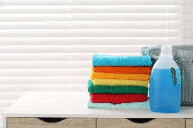 Çamaşır sepetinde havlular ve bir şişe deterjan var. Kapalı pencerenin yanındaki beyaz masada. Mesaj atmak için yer var.