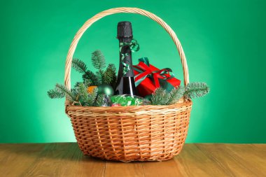 Bir şişe köpüklü şarap ve sepetteki Noel dekoru yeşil arka planda, ahşap masada. Kutlama hediyesi.