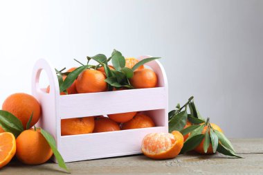 Tahta masadaki sandıkta taze mandalina ve yeşil yapraklar.