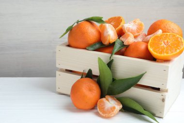 Taze mandalina ve yeşil yapraklar beyaz ahşap masada, yakın plan. Metin için boşluk