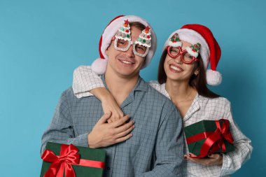 Noel Baba şapkalı ve pijamalı mutlu çift açık mavi arka planda Noel hediyeleri