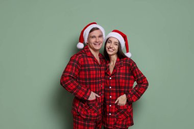 Gri yeşil arka planda Noel Baba şapkalı ve pijamalı mutlu bir çift. Noel atmosferi