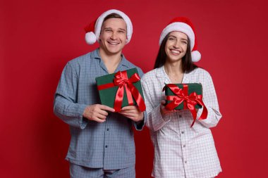 Kırmızı arka planda Noel Baba şapkalı mutlu çift