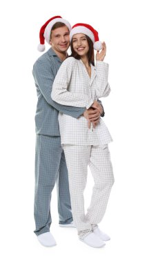 Beyaz arka planda Noel Baba şapkalı ve pijamalı mutlu bir çift. Noel atmosferi