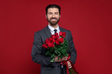 Sevgililer Günü. Kırmızı arka planda gül buketi olan yakışıklı adam.