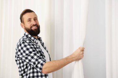 Evde pencere perdelerini asan adam, düşük açılı görüntü.