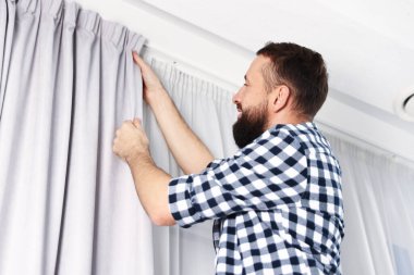Evde pencere perdelerini asan adam, düşük açılı görüntü.