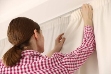 Kadın pencerenin perdelerini asıyor, düşük açılı.