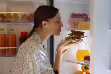 Açık buzdolabının yanında lezzetli sandviçleri olan bir kadın.