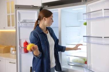 Mutfakta içi boş buzdolabının yanında limonlu bir kadın.
