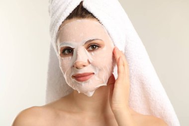 Saçları havluya sarılı ve açık gri arka planda maske takan bir kadın.