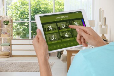 Akıllı ev sistemi. Tablet bilgisayarındaki uygulamayı kullanarak odadaki ev özelliklerini kontrol eden kadın, kapat
