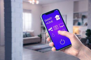 Akıllı ev sistemi. Oda özelliklerini kontrol etmek için cep telefonundaki uygulamayı kullanan adam, yakın plan