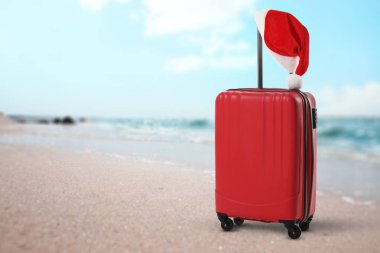 Noel tatili. Kumsalda deniz kenarında Noel Baba şapkalı bavul.