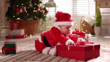 Noel Baba kostümlü şirin bir bebek. Evde Noel hediyeleri ve dekoru var.